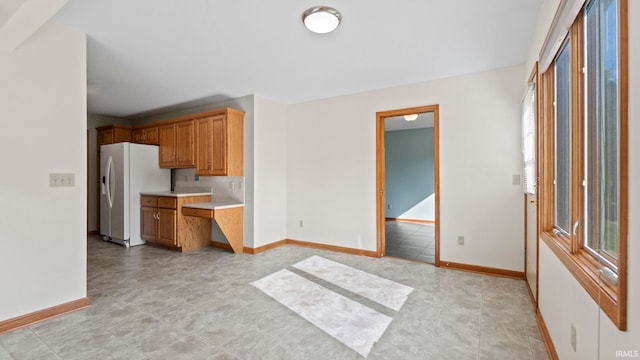 kitchen featuring brown cabinets, white fridge with ice dispenser, baseboards, and light countertops