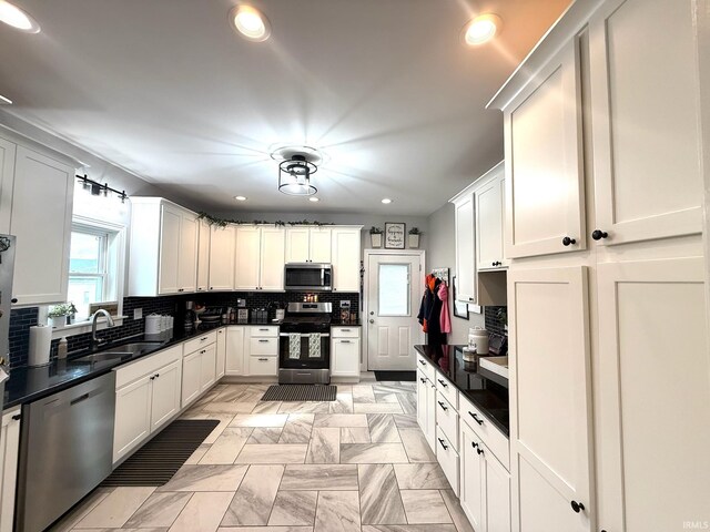 kitchen featuring a sink, white cabinetry, appliances with stainless steel finishes, decorative backsplash, and dark countertops