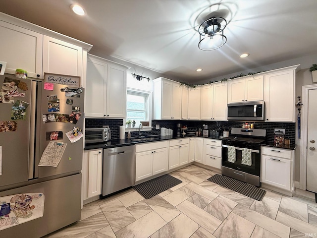 kitchen with stainless steel appliances, a sink, white cabinetry, decorative backsplash, and dark countertops