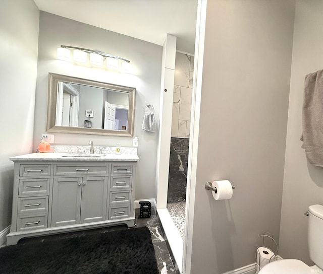 bathroom featuring baseboards, a tile shower, vanity, and toilet