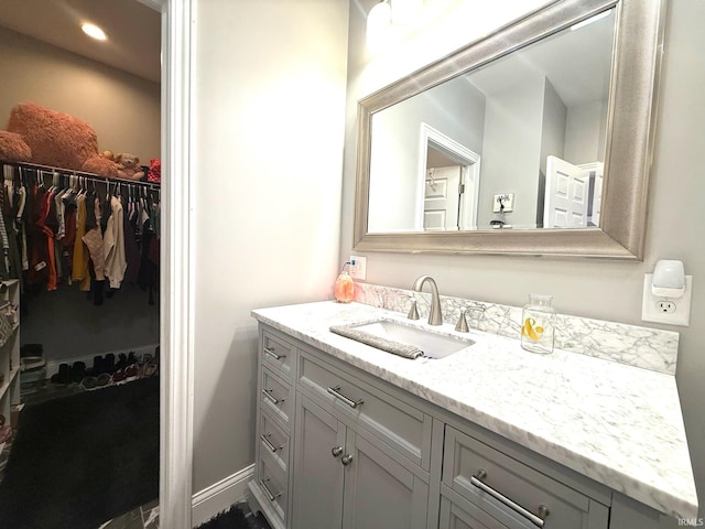 bathroom featuring a walk in closet, vanity, baseboards, and recessed lighting