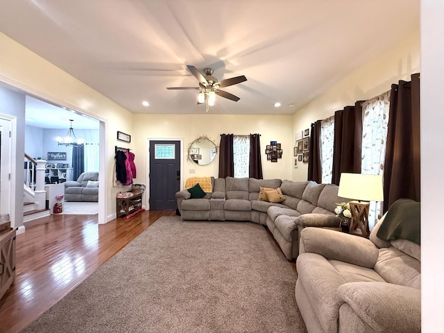 living room with ceiling fan with notable chandelier, wood finished floors, recessed lighting, and stairs