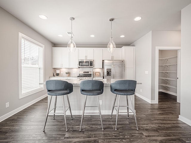 kitchen with dark wood-style flooring, appliances with stainless steel finishes, white cabinets, a kitchen island with sink, and baseboards