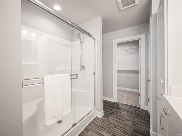 bathroom featuring a spacious closet, visible vents, a shower stall, and wood finished floors