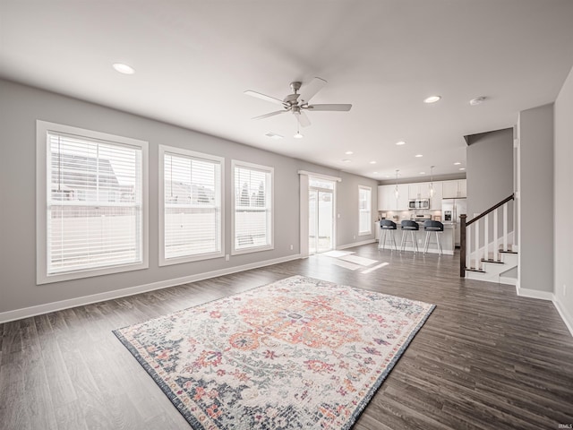 unfurnished living room with dark wood finished floors, recessed lighting, ceiling fan, baseboards, and stairs