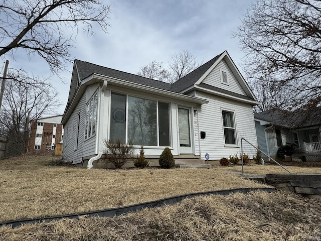 rear view of property featuring a sunroom, a shingled roof, and a yard