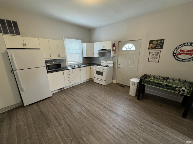 kitchen with white appliances, visible vents, dark countertops, dark wood-type flooring, and under cabinet range hood