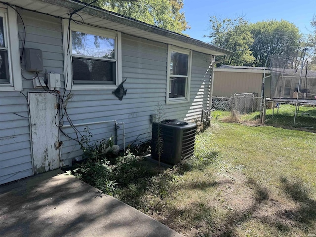 view of side of home with a lawn, a trampoline, fence, and cooling unit