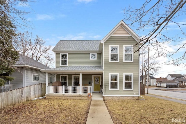 traditional-style house featuring covered porch, a shingled roof, a front yard, and fence