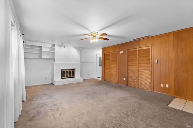 unfurnished living room featuring visible vents, a brick fireplace, carpet flooring, ceiling fan, and wooden walls