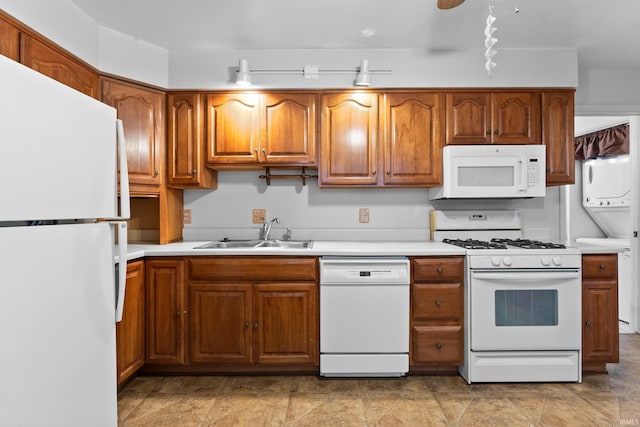 kitchen featuring brown cabinets, stacked washer and dryer, light countertops, a sink, and white appliances