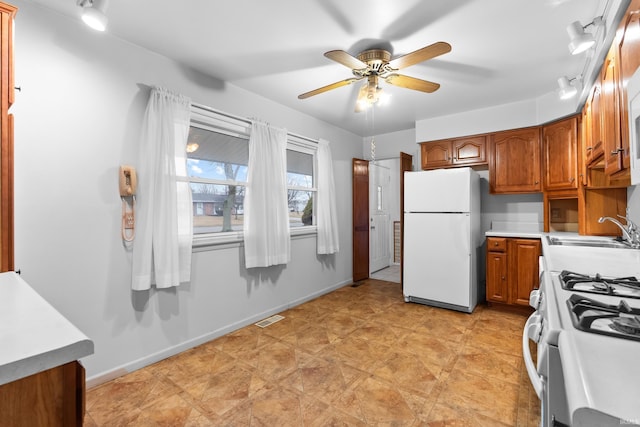 kitchen with brown cabinetry, white appliances, a sink, and baseboards