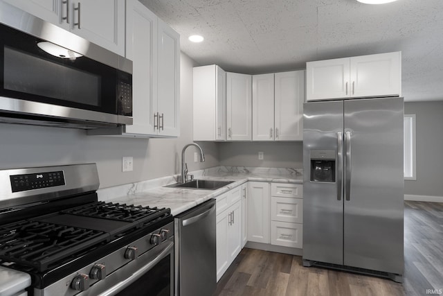 kitchen with light stone counters, dark wood finished floors, appliances with stainless steel finishes, white cabinets, and a sink