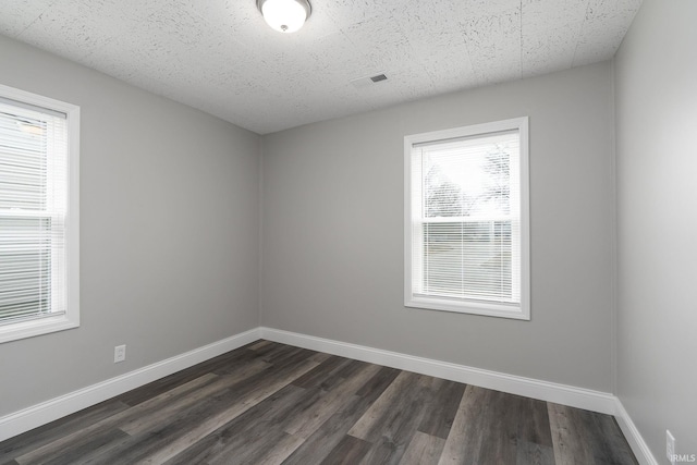 empty room featuring dark wood-style flooring, visible vents, and baseboards