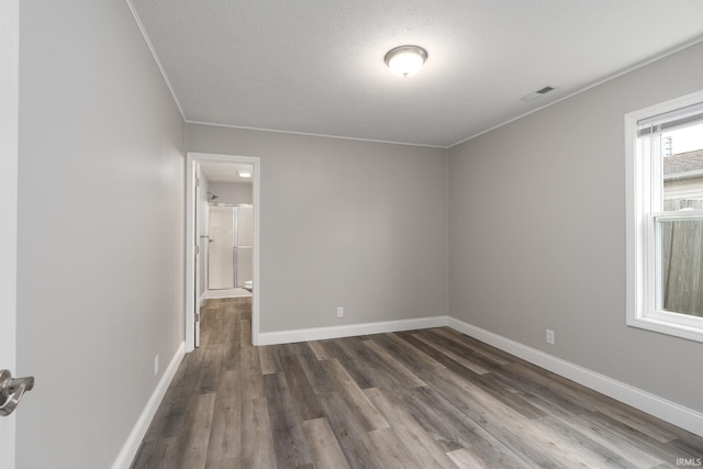 empty room featuring visible vents, baseboards, dark wood finished floors, ornamental molding, and a textured ceiling