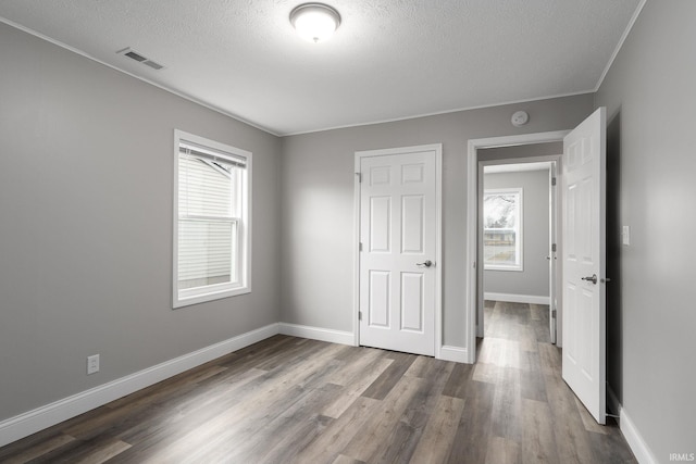 unfurnished bedroom featuring dark wood-style flooring, multiple windows, visible vents, and baseboards