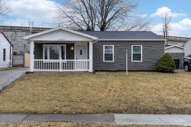 view of front of property featuring covered porch, stone siding, a shingled roof, and a front yard