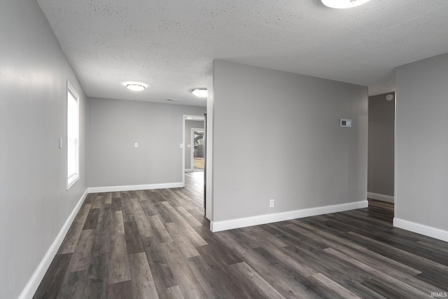 empty room with dark wood finished floors, a textured ceiling, and baseboards