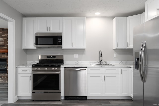 kitchen featuring dark wood-style flooring, a sink, white cabinetry, appliances with stainless steel finishes, and light stone countertops