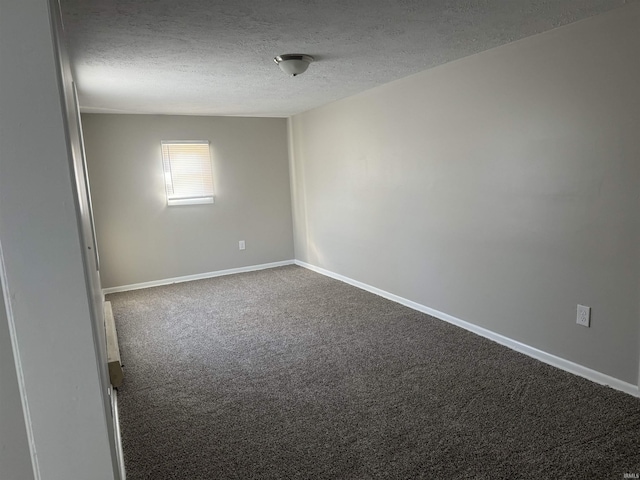 empty room featuring dark carpet, a textured ceiling, and baseboards