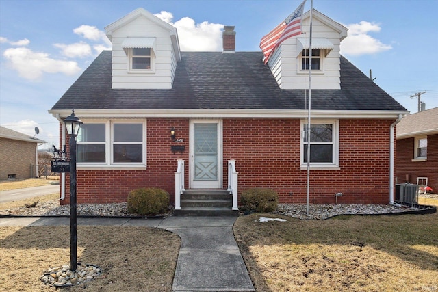 view of front facade featuring entry steps, brick siding, a chimney, and central air condition unit