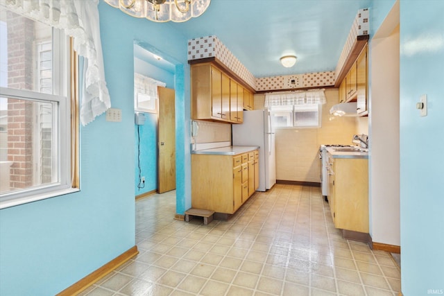 kitchen with white appliances, under cabinet range hood, baseboards, and light countertops