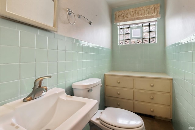 half bathroom featuring toilet, tile walls, a sink, and wainscoting