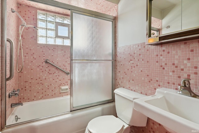 bathroom featuring toilet, tile walls, bath / shower combo with glass door, and a sink