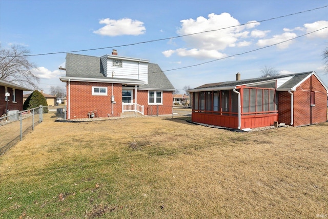 back of property with a lawn, a sunroom, a chimney, fence, and brick siding