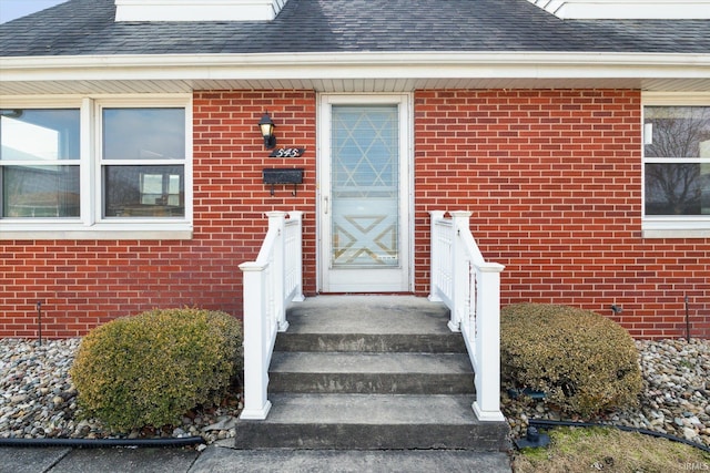 view of exterior entry featuring a shingled roof and brick siding