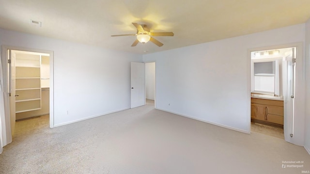 unfurnished bedroom featuring baseboards, connected bathroom, light colored carpet, a spacious closet, and a closet