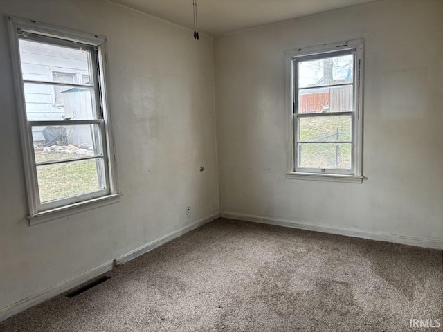 empty room featuring carpet floors, a healthy amount of sunlight, baseboards, and visible vents