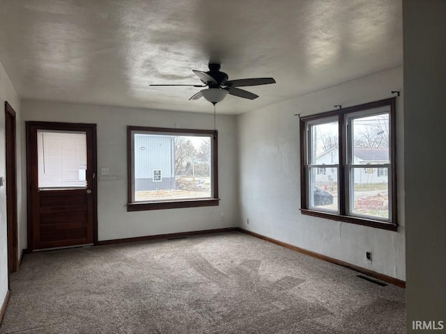 carpeted empty room featuring baseboards, visible vents, and ceiling fan