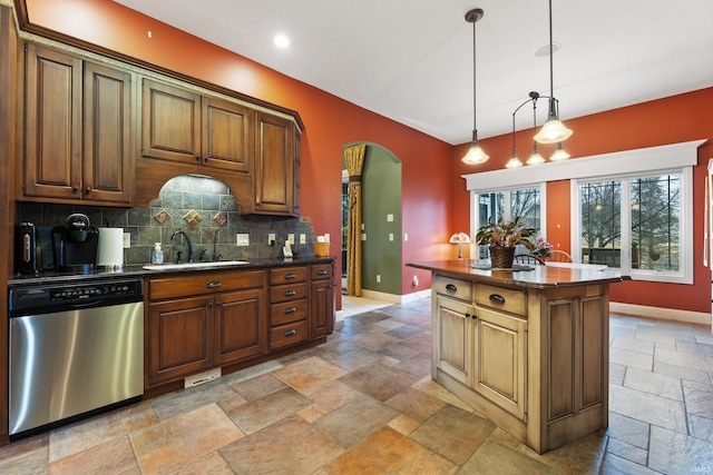 kitchen with stone tile floors, arched walkways, dark countertops, stainless steel dishwasher, and a sink