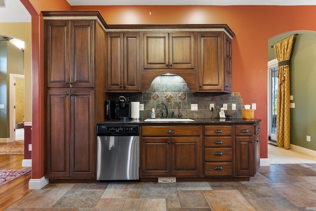 kitchen with arched walkways, decorative backsplash, dishwasher, stone finish floor, and a sink