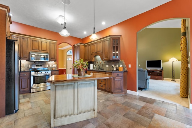 kitchen featuring appliances with stainless steel finishes, arched walkways, a center island, and brown cabinets