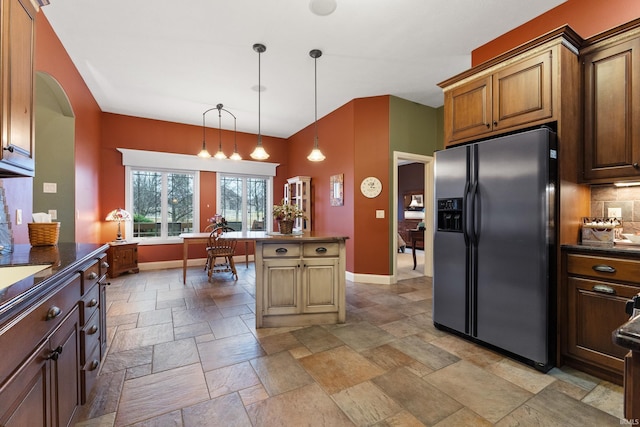 kitchen with arched walkways, baseboards, fridge with ice dispenser, stone tile flooring, and backsplash