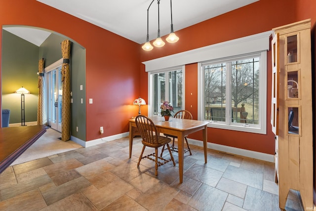 dining room with baseboards, arched walkways, and stone finish flooring