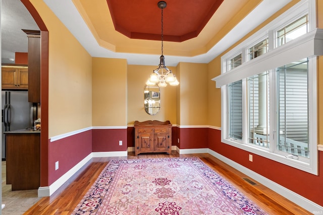 unfurnished dining area with wood finished floors, a raised ceiling, and baseboards