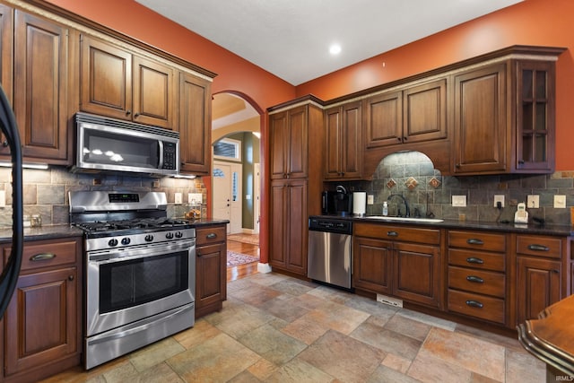 kitchen featuring appliances with stainless steel finishes, arched walkways, a sink, and backsplash