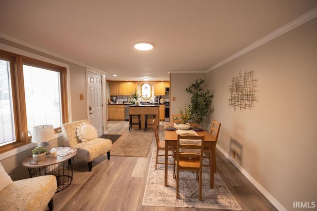 dining room featuring light wood-style flooring, ornamental molding, and baseboards