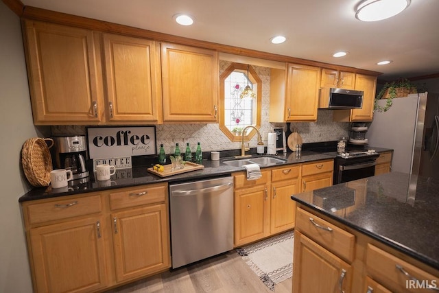 kitchen featuring light wood-style flooring, decorative backsplash, appliances with stainless steel finishes, a sink, and dark stone counters