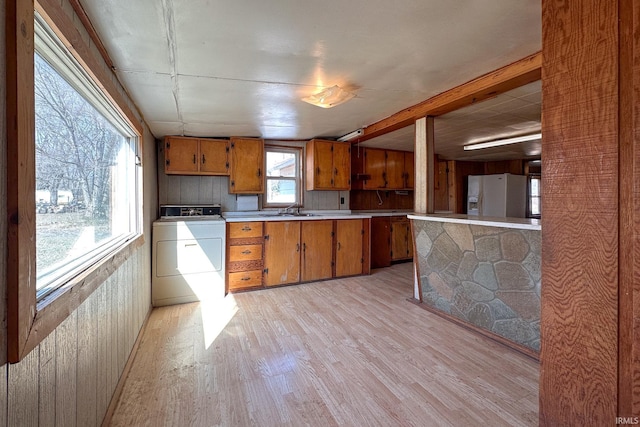 kitchen featuring a sink, light wood-style floors, brown cabinets, white fridge with ice dispenser, and washer / clothes dryer