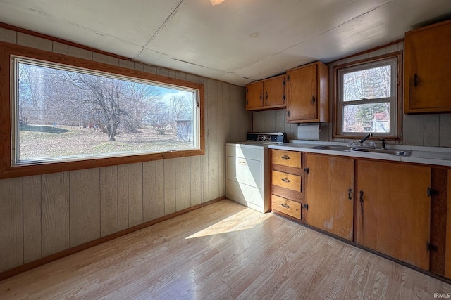 kitchen featuring light wood-style flooring, washer / clothes dryer, brown cabinets, vaulted ceiling, and a sink