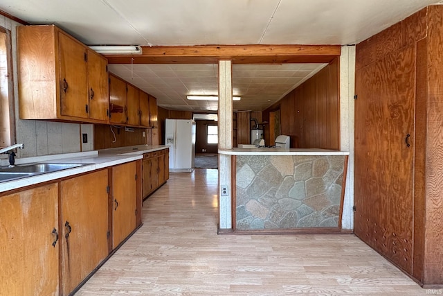 kitchen featuring light wood-style flooring, white refrigerator with ice dispenser, brown cabinetry, and a sink