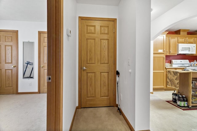 hall featuring arched walkways, baseboards, and light colored carpet