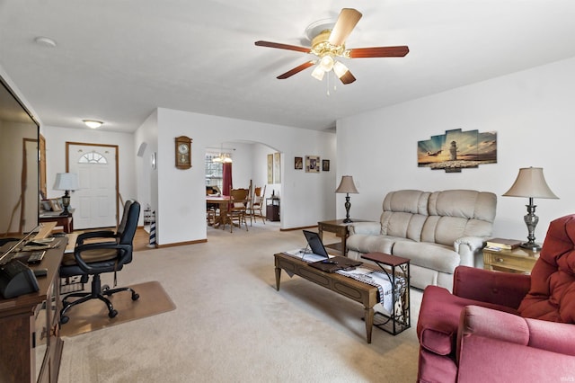 living room featuring ceiling fan, arched walkways, baseboards, and light colored carpet