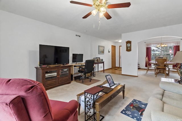 carpeted living room with arched walkways, ceiling fan with notable chandelier, visible vents, and baseboards