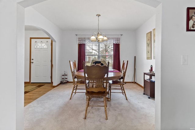 dining space with light carpet, baseboards, a chandelier, and arched walkways