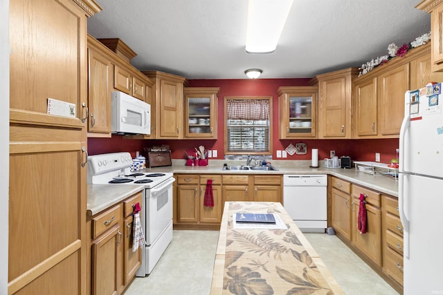 kitchen featuring white appliances, glass insert cabinets, light countertops, and a sink